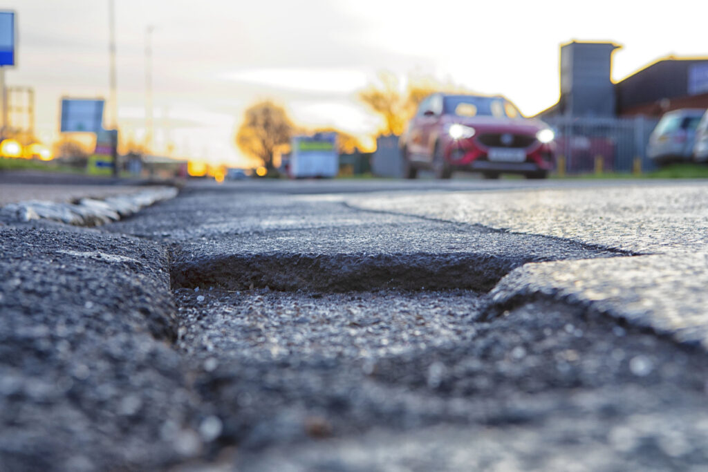 Pothole in road with red vehicle approaching