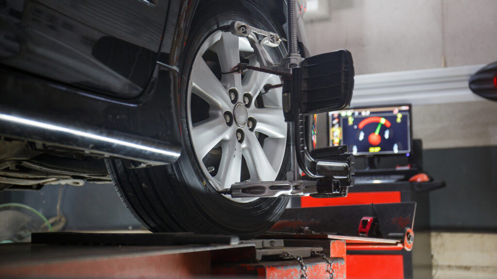 Black car on stand for wheel alignment check.